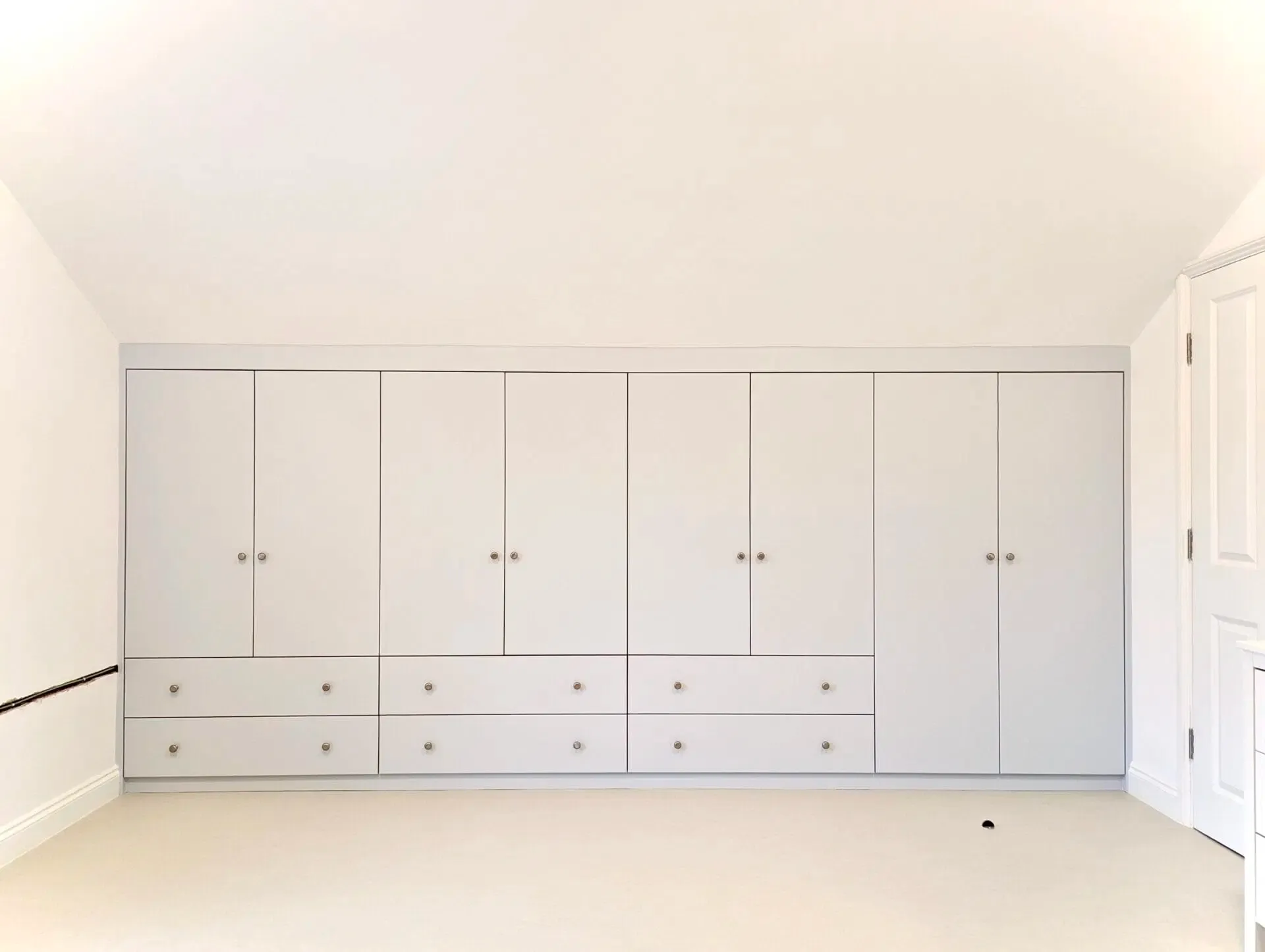 White fitted wardrobe with multiple doors and drawers in a room with light-colored walls and carpet.