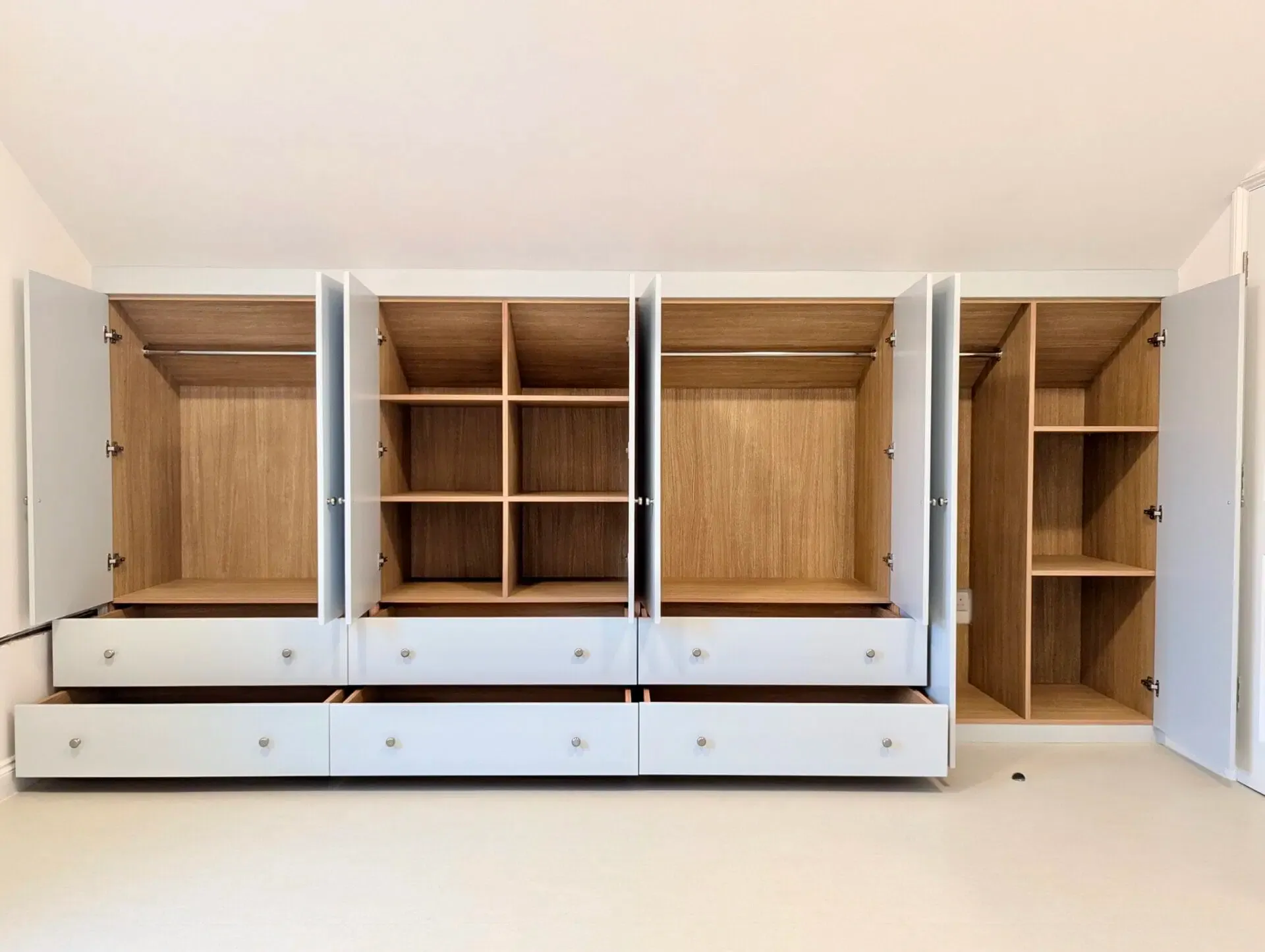 Empty white wardrobe with open doors and drawers, showing shelves and clothing rods.