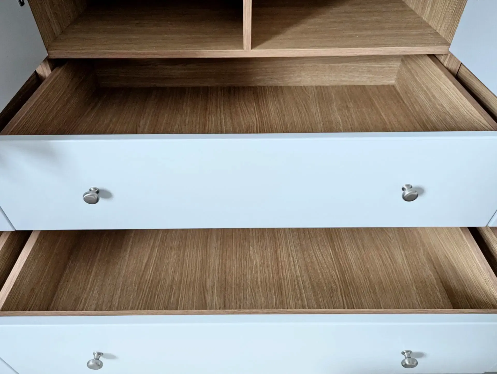 White dresser with two open drawers, brown interior, silver knobs.