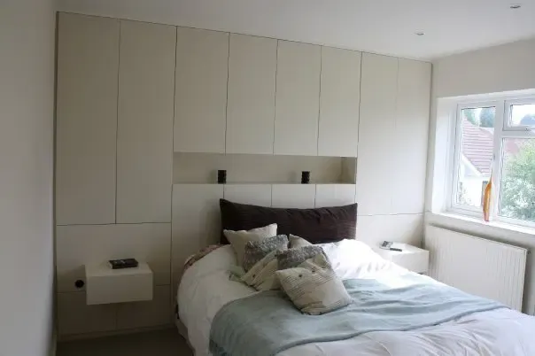 Bedroom with built-in cream-colored cabinets, bed with pillows, and window.