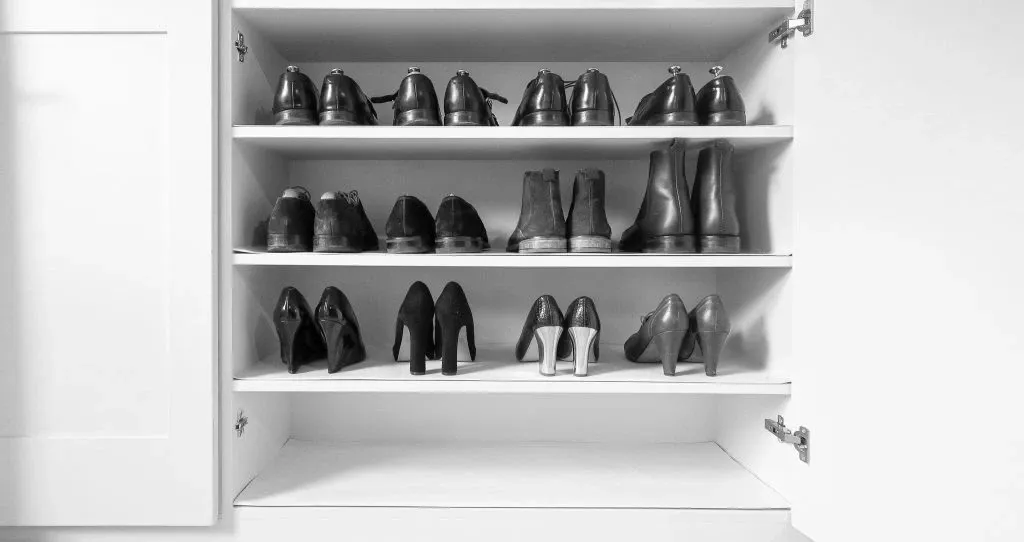 Shoe cabinet with three shelves. Each shelf displays pairs of black shoes.