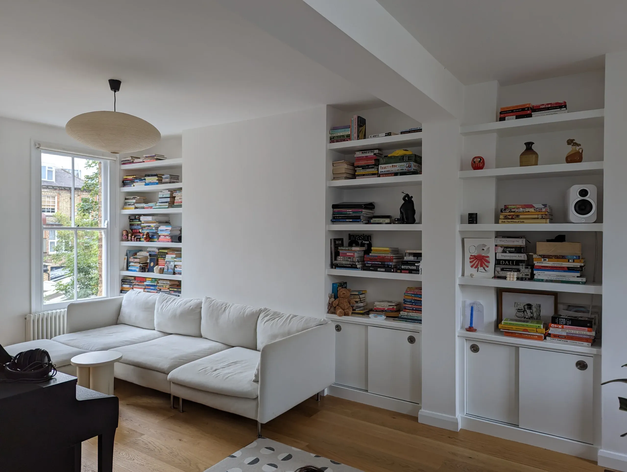 Living room with white sofa, built-in shelves filled with items, and a window.