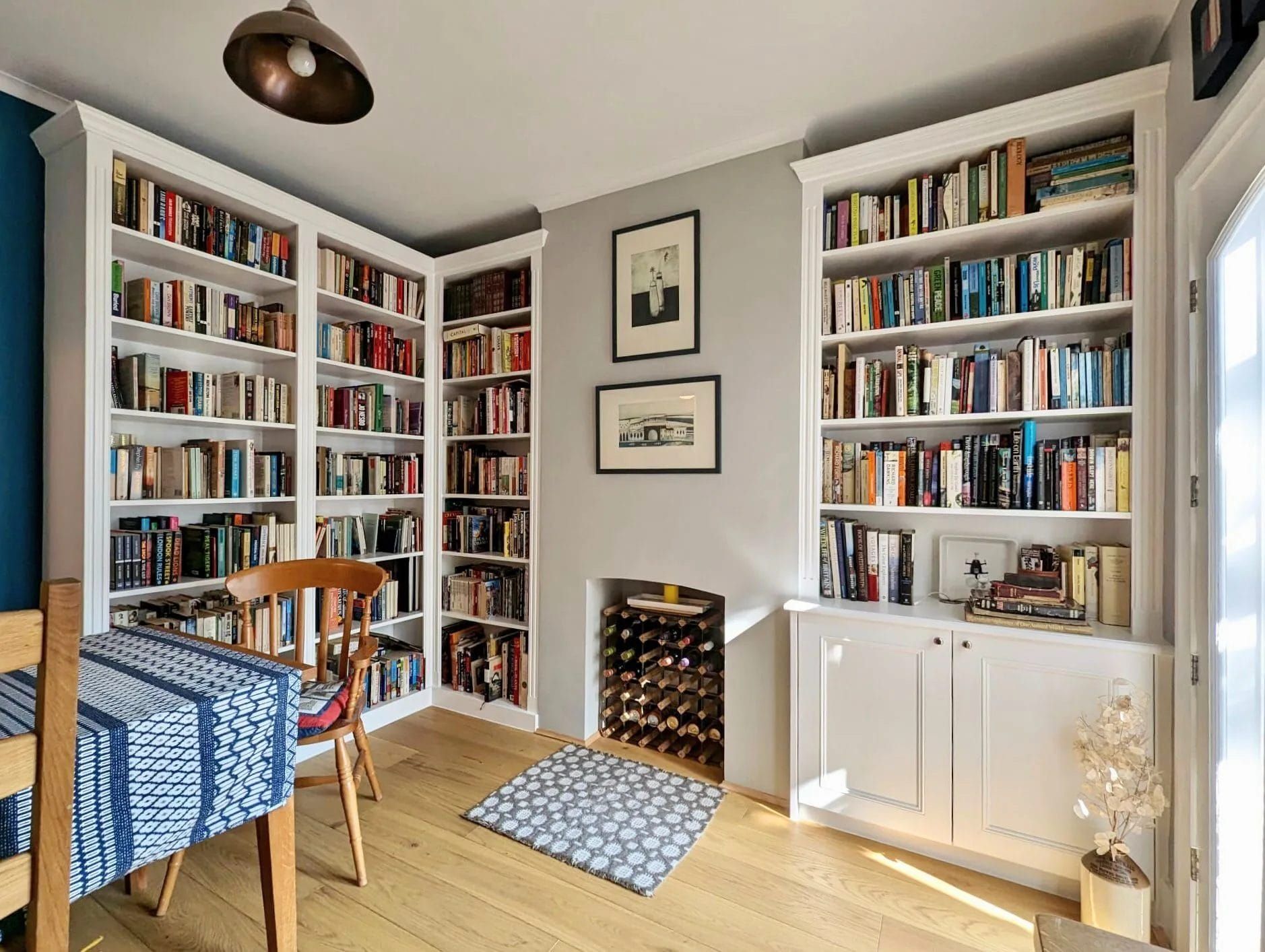 Room with built-in white bookshelves filled with books, a wine rack, and a wooden floor.