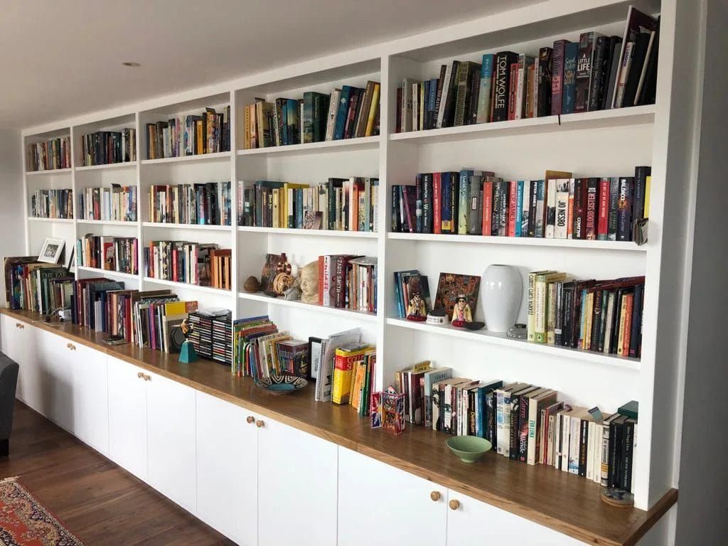 White built-in bookshelves filled with books and decorative items, above a row of white cabinets.