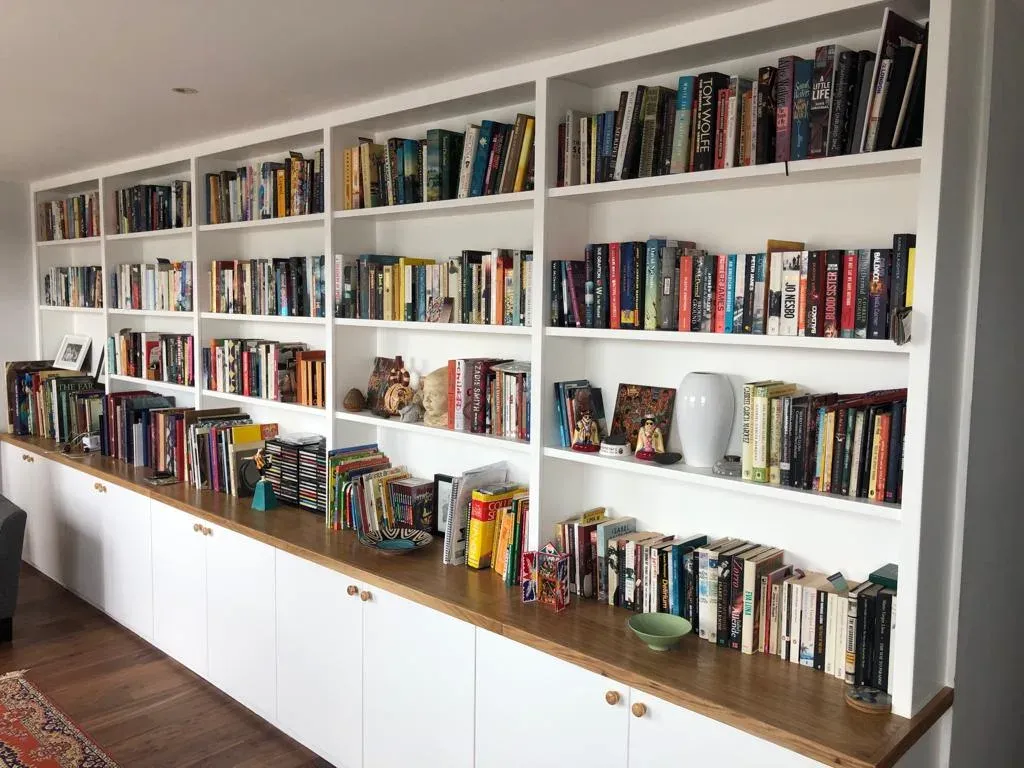White built-in bookshelves filled with books, spanning a wall; bottom cabinets below.