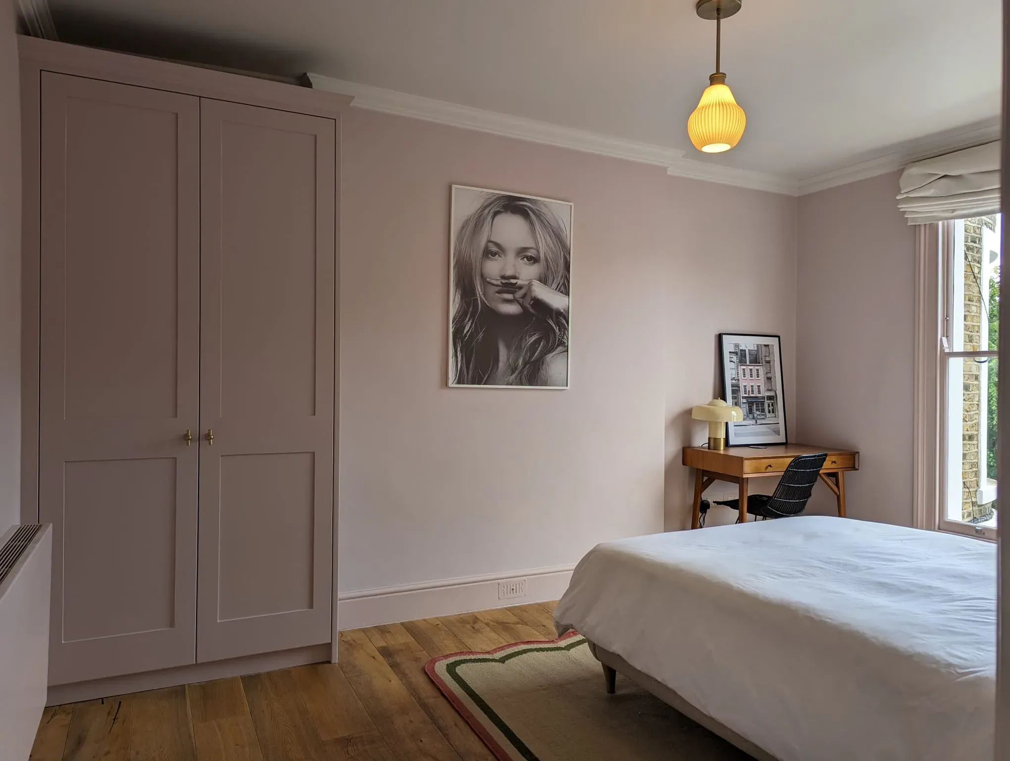 Bedroom with pink walls, closet, and a bed. Art and desk visible.