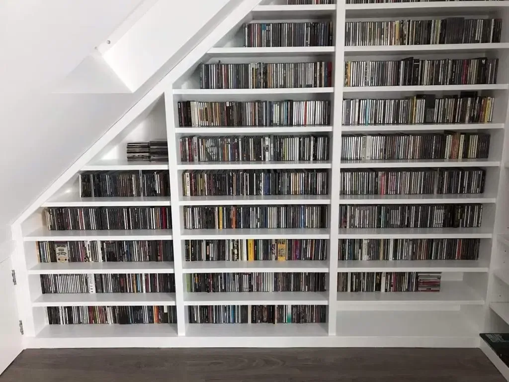 White built-in shelves filled with CDs under a sloped ceiling.