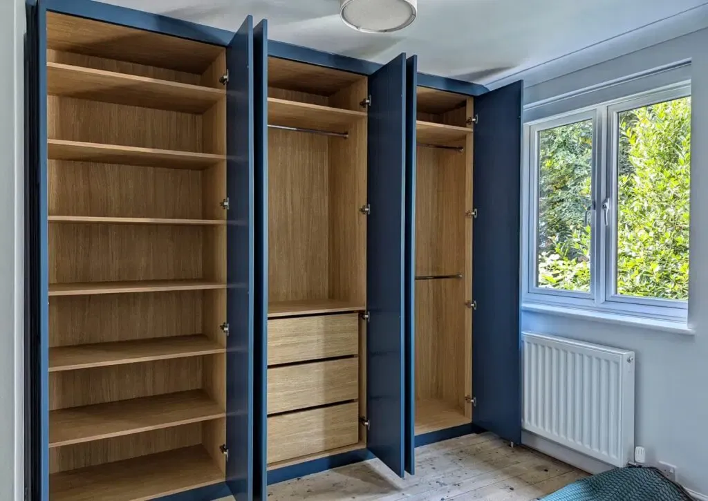 Blue built-in wardrobe with open doors revealing shelves, hanging space, and drawers; inside is light wood.