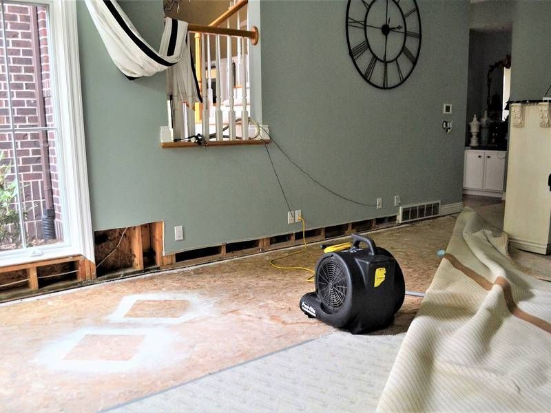 A living room with a clock on the wall and a fan on the floor.