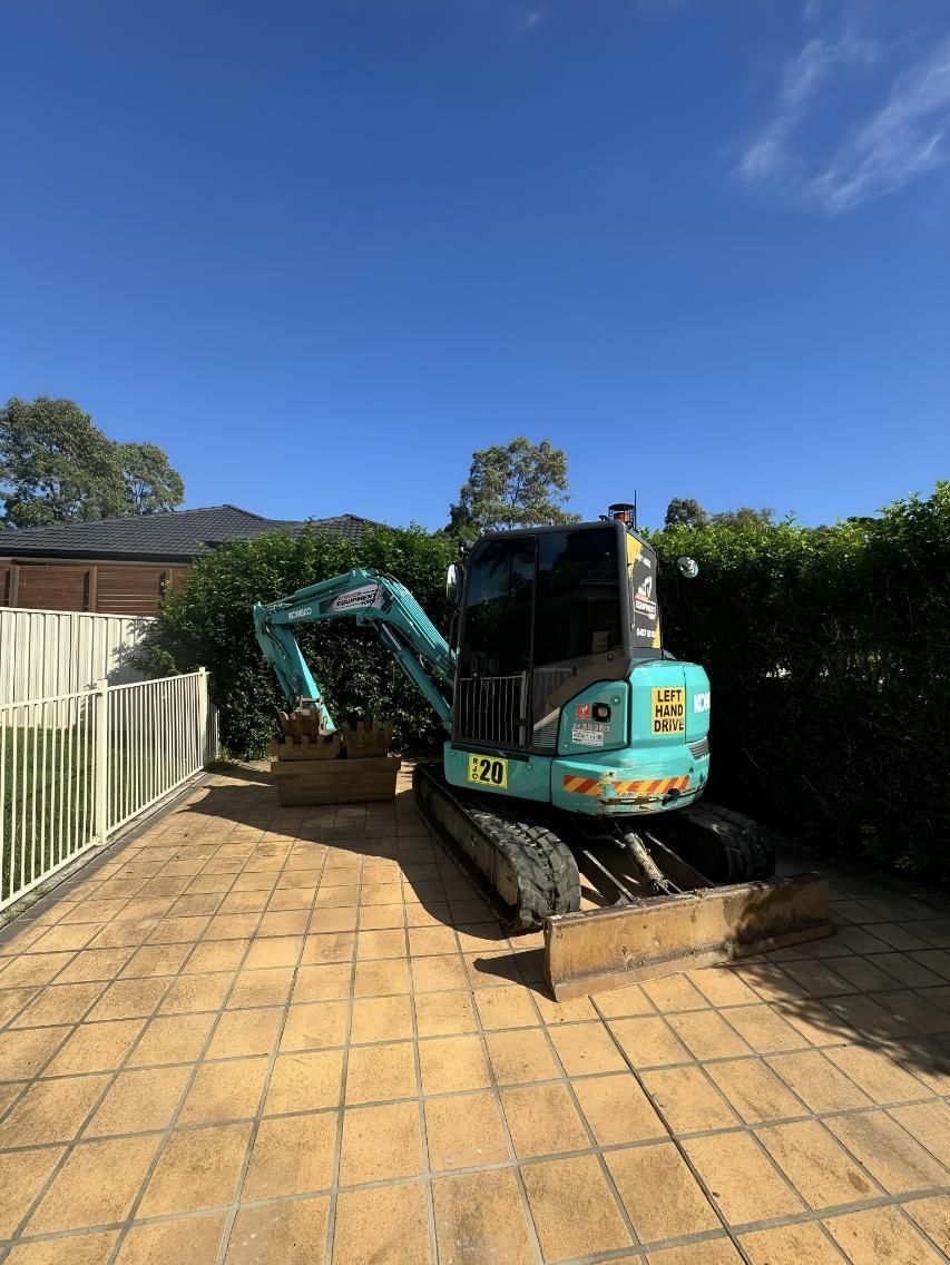 A Small Excavator Is Parked in A Driveway — R&J Cronin Equipment Hire in Bonnells Bay, NSW