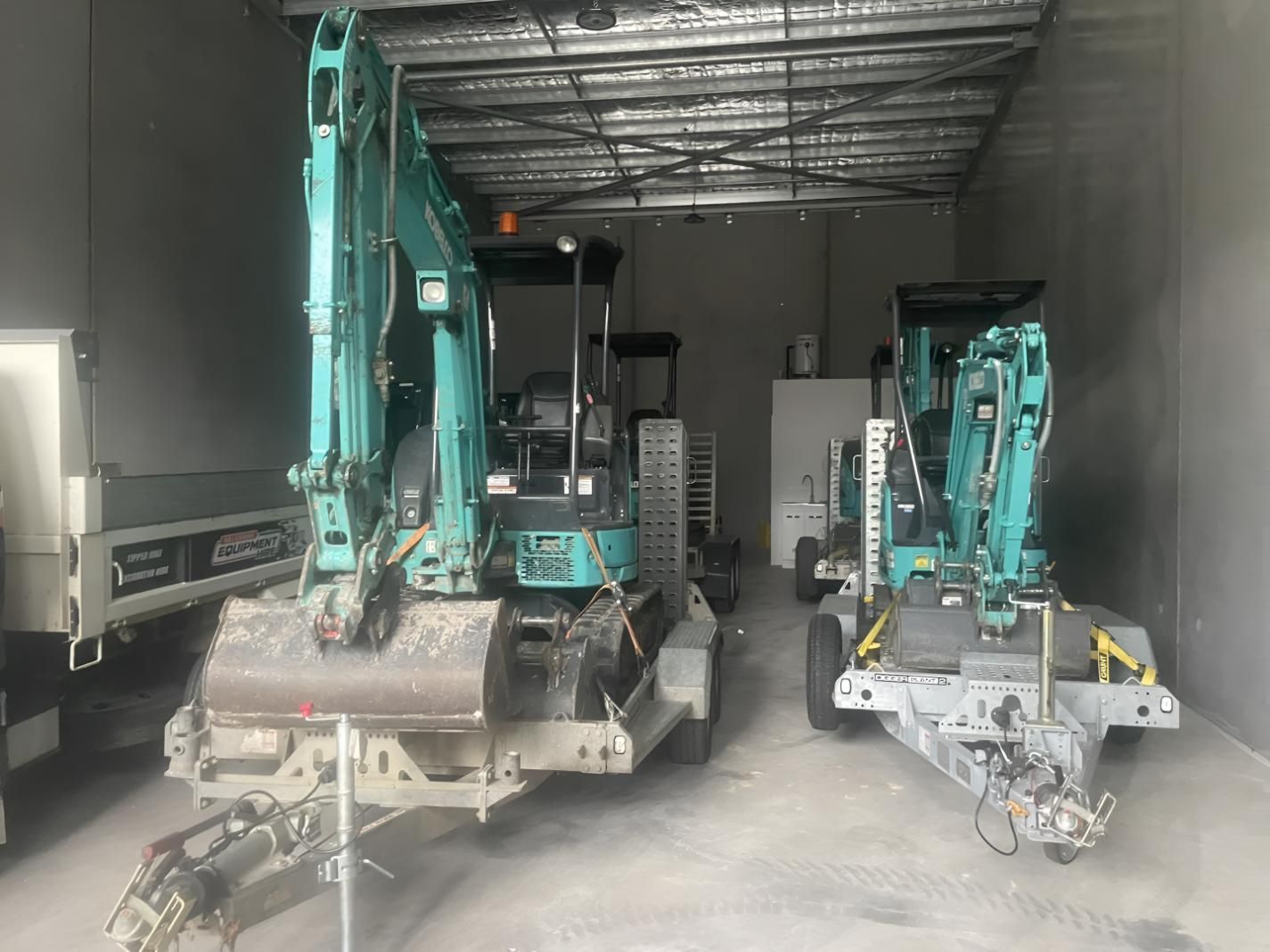 Two Excavators Are Parked in A Garage — R&J Cronin Equipment Hire in Bonnells Bay, NSW