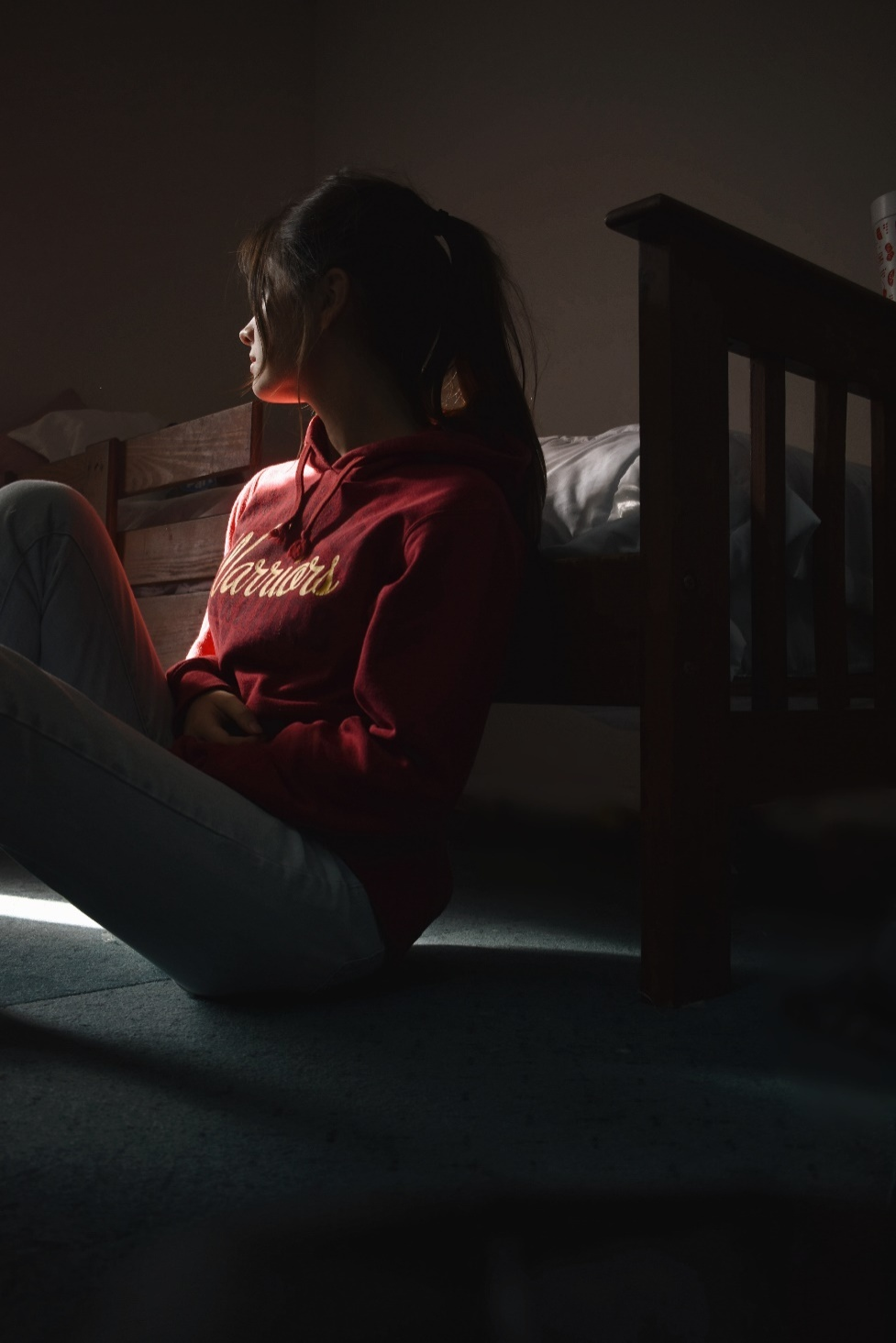 Person in a red sweater sits on the floor beside a staircase in dim light.