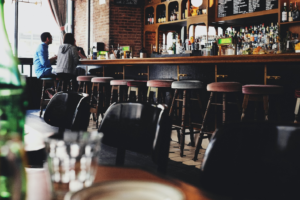 Empty bar interior with stools, bottles on shelves, and a person near the window