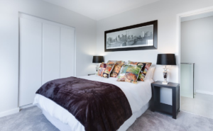 Bright bedroom with white bed, dark throw, patterned pillows, and framed wall art.