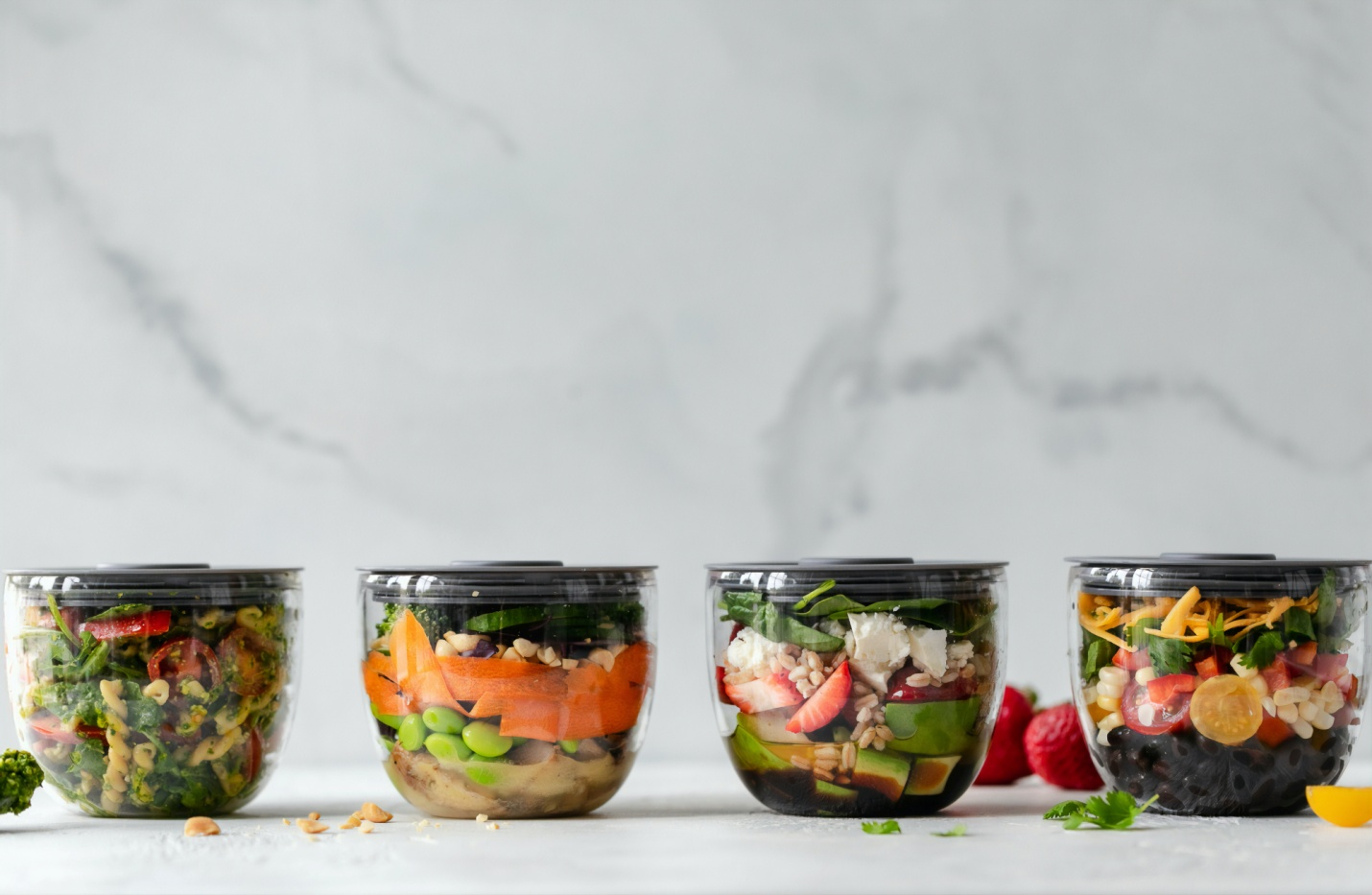 Four jars of colorful layered salad with vegetables and fruit on a white surface