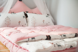Pink floral bedding with a quilt on a bed beneath a sheer canopy