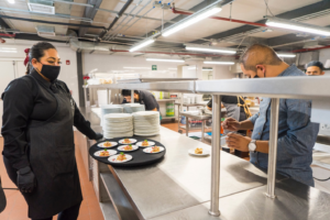 Chef and diner at a cafeteria counter, with trays of food on display