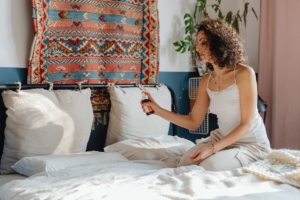 Woman sitting on a bed, holding a remote in a bright bedroom with patterned wall decor.