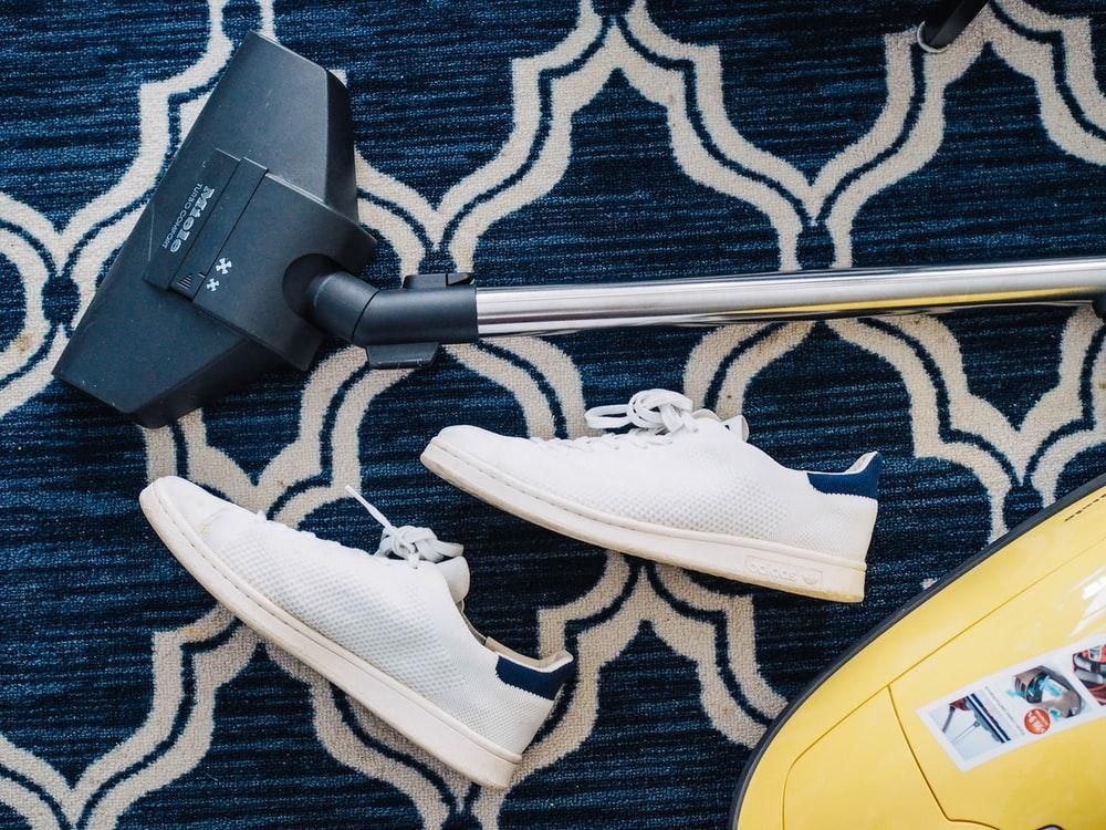 Vacuum, two white sneakers, and a yellow object on a blue patterned rug