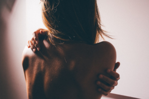 Person seen from behind, hugging their shoulders in soft warm light