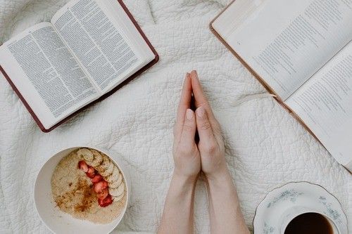 Hands clasped in prayer near open books and a bowl of oatmeal.