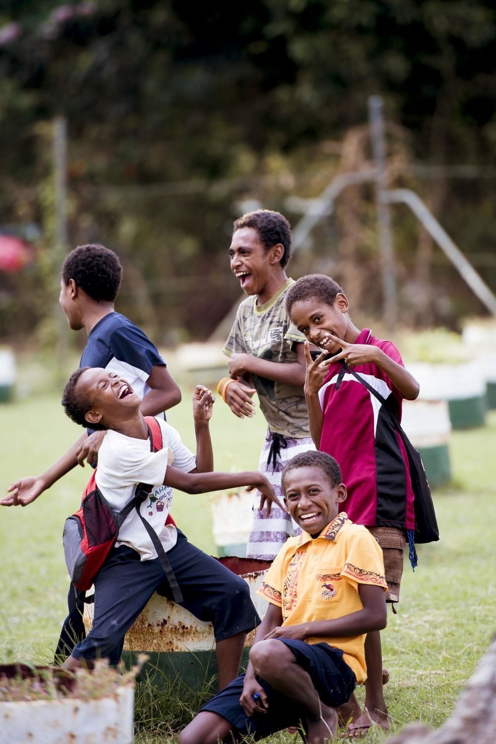Five children laughing and playing outdoors on a grassy field.