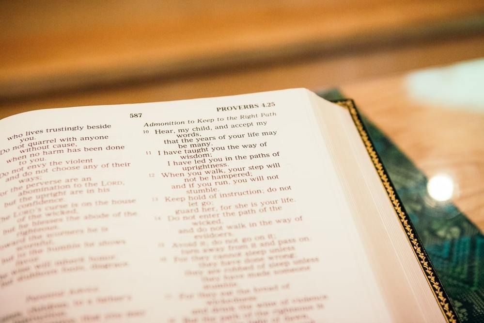 An open Bible showing text from the book of Proverbs, with the page angled in soft lighting.