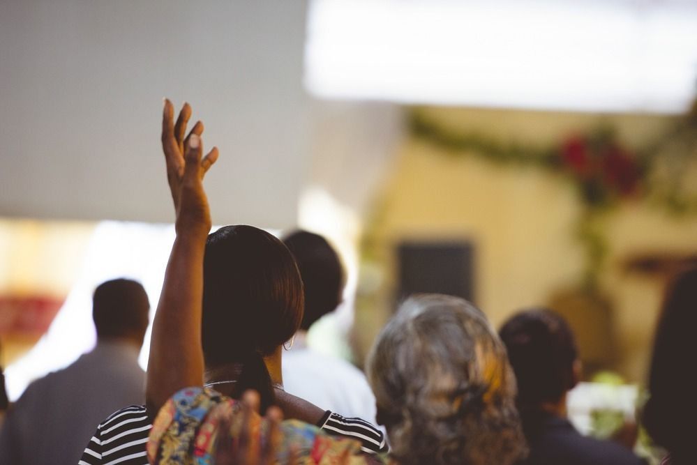 Audience members in a dimly lit room with one person raising their hand, likely at a conference or gathering.