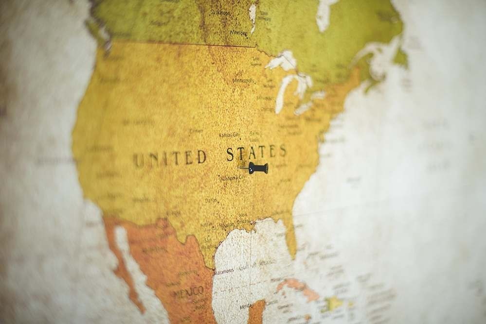 A vintage-style map of North America with a black pushpin centered on the United States.