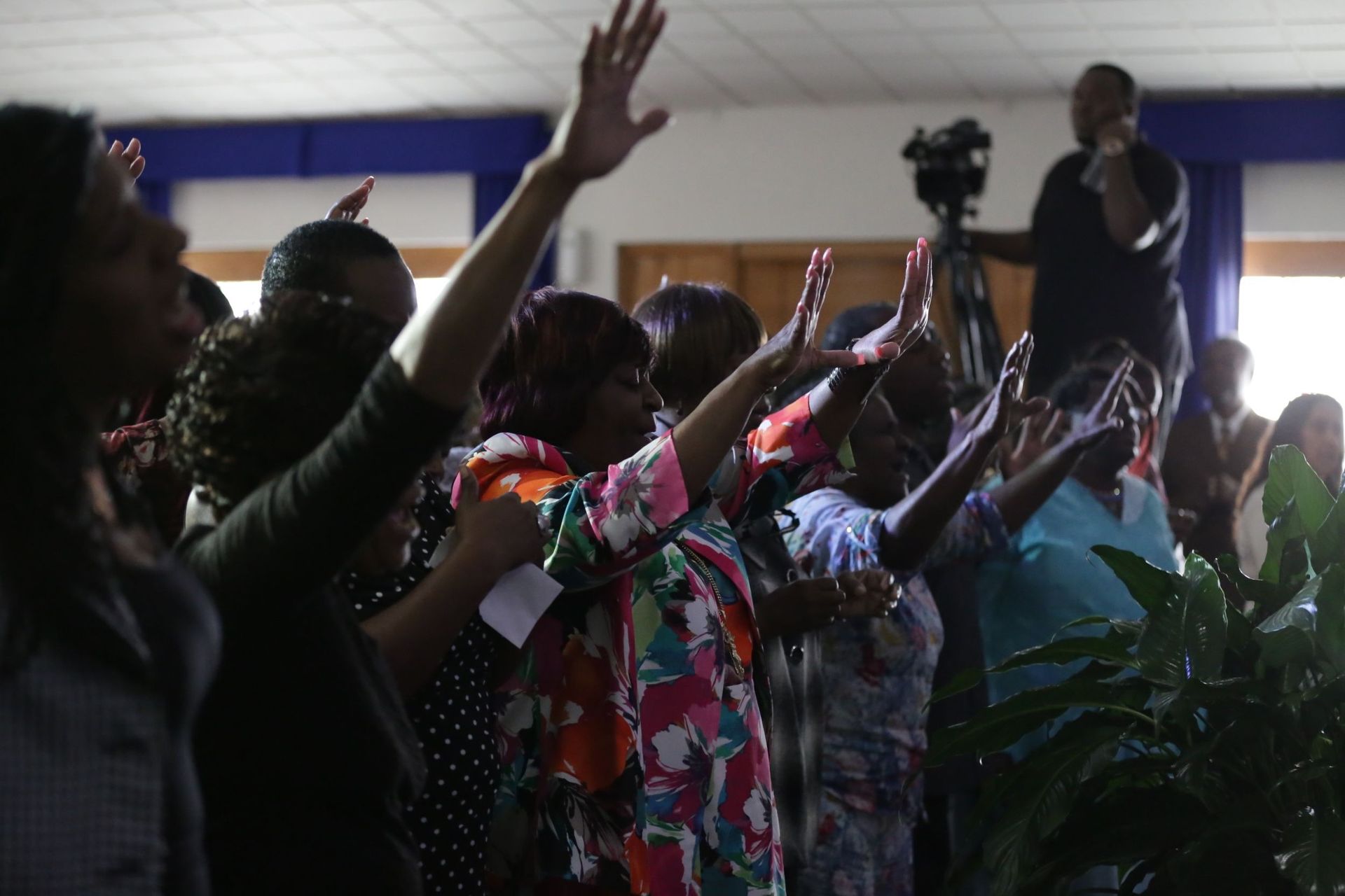 A group of people standing in a room with hands raised in a gesture of worship or prayer.
