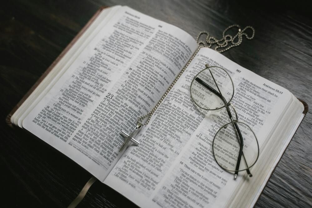 Open Bible with a cross necklace and eyeglasses resting on the pages.