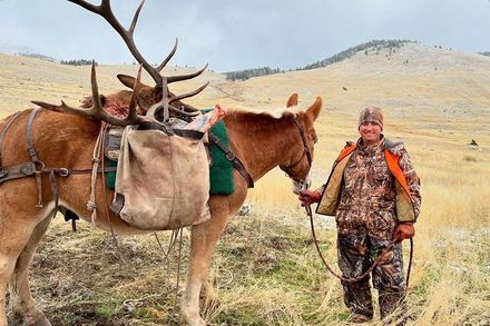 A man is standing next to a horse with antlers on it.