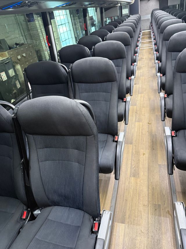 Rows of gray seats inside a bus or train, viewed down a narrow aisle.