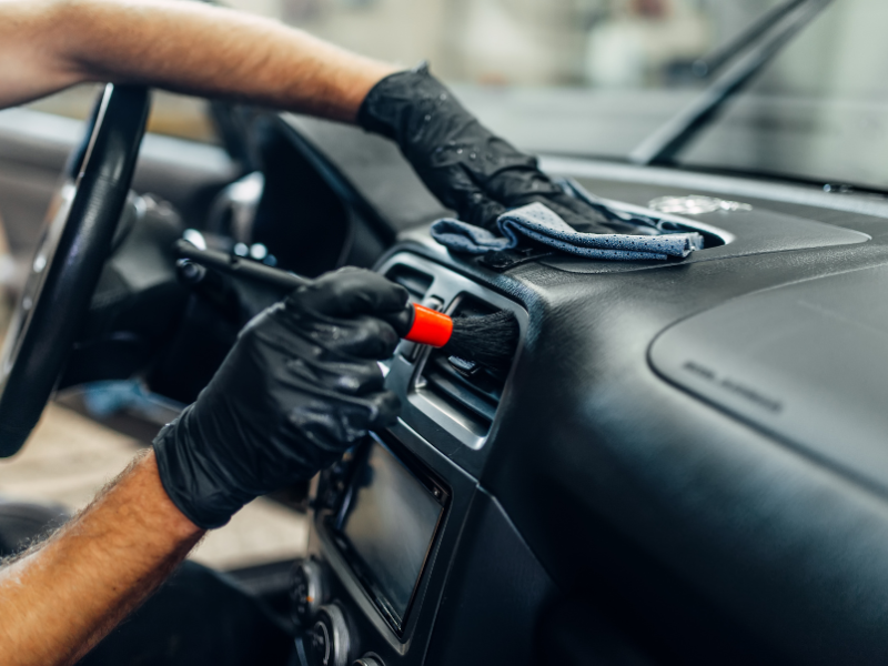 Gloved hands cleaning a car dashboard with a cloth and spray nozzle