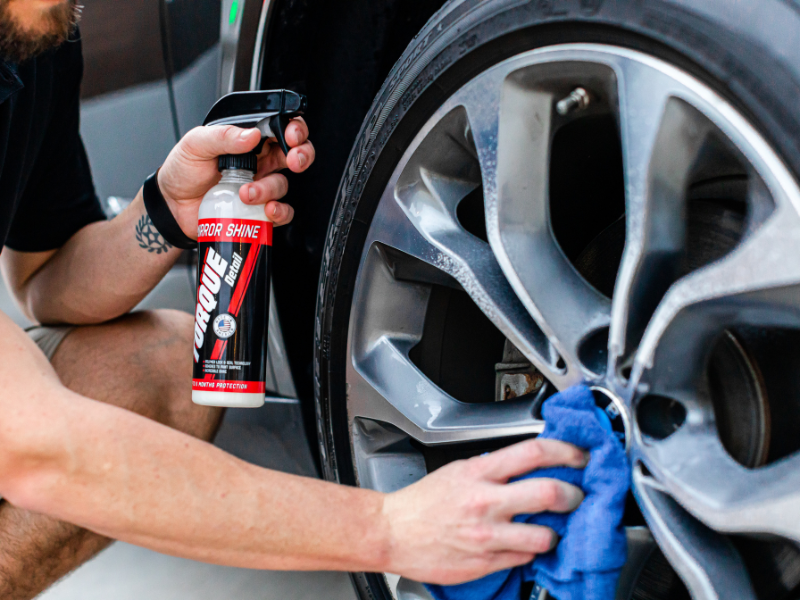Person cleaning a car wheel with a blue cloth while holding a tire cleaner spray can