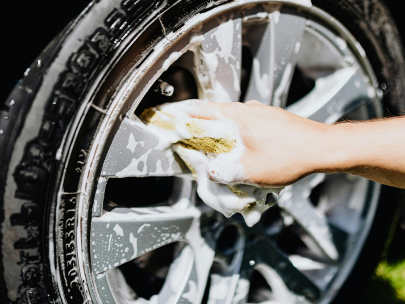 Hand washing a car wheel with soapy water and a sponge
