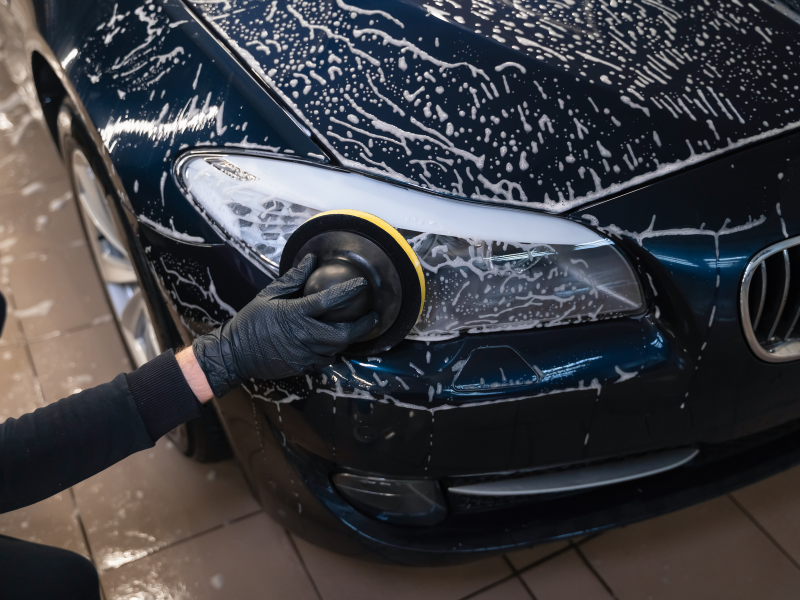 Person polishing a black car hood with a black cloth, creating foam and water streaks.
