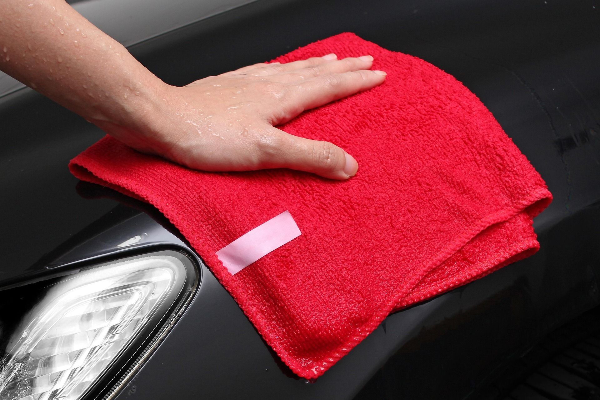 Hand wiping a black car hood with a red microfiber cloth