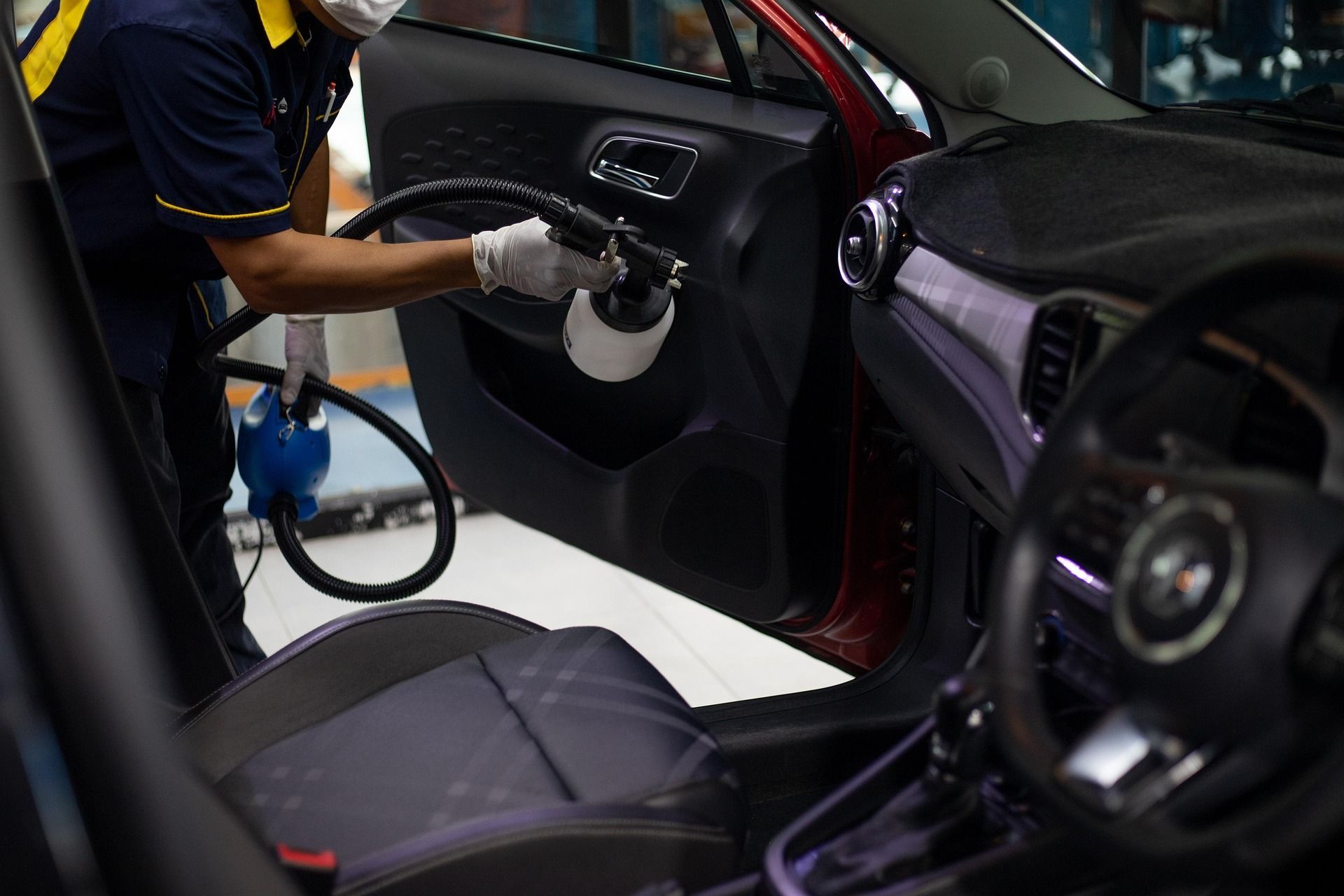 Technician cleaning a black car’s interior door panel with a steam vacuum.