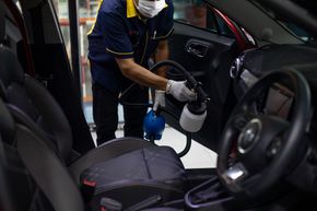 Worker disinfecting a car interior with a spray bottle and cloth Worker sanitizing the interior of a car with a spray bottle and cloth