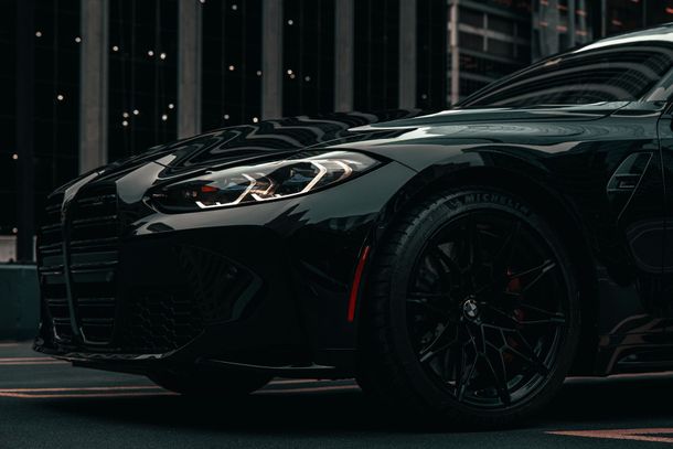 Black sports car parked at night on a city street, front view with glossy paint and lit headlights