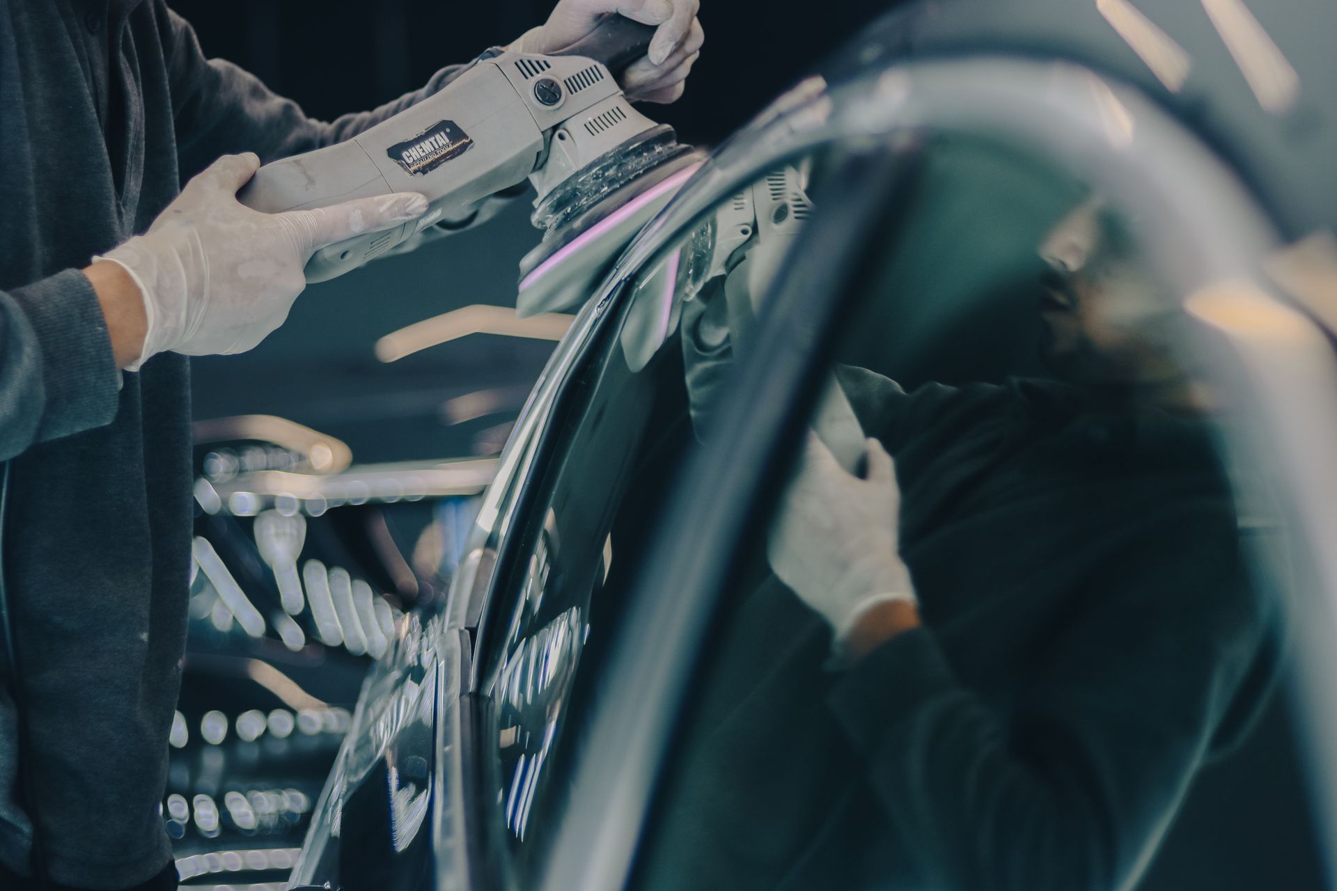 Worker using an electric tool on a car door in a dim auto repair shop