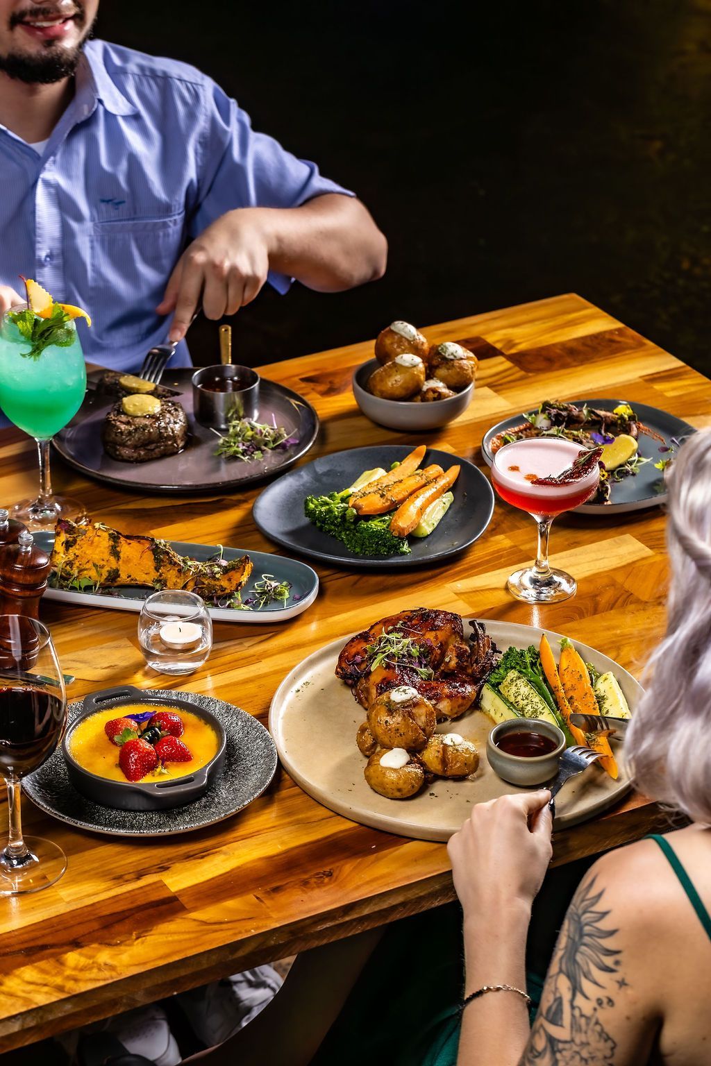 Overhead shot of a table with steak, sauce, salads, and creme brulee dishes.