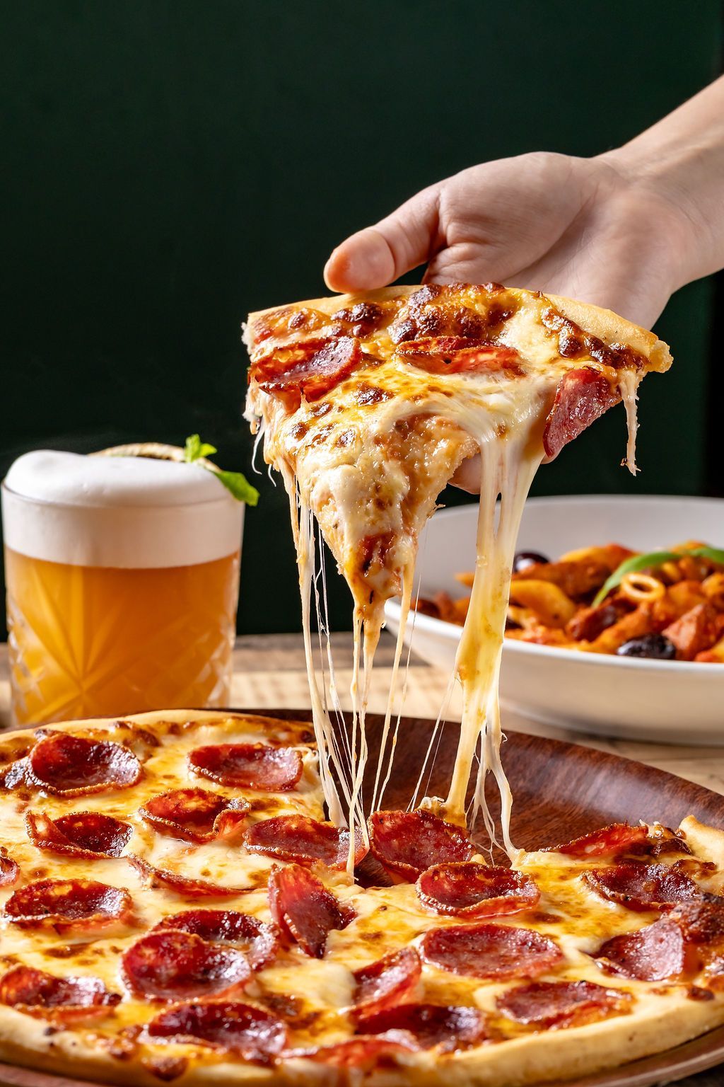 Person lifting a slice of pizza with toppings from a wooden board.