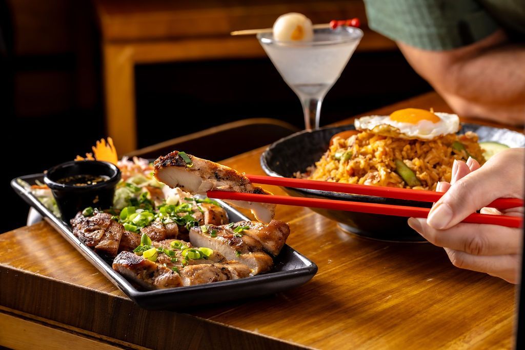 Bowls of food and drinks on a wooden board. The dishes are on a black and white patterned towel at the beach.