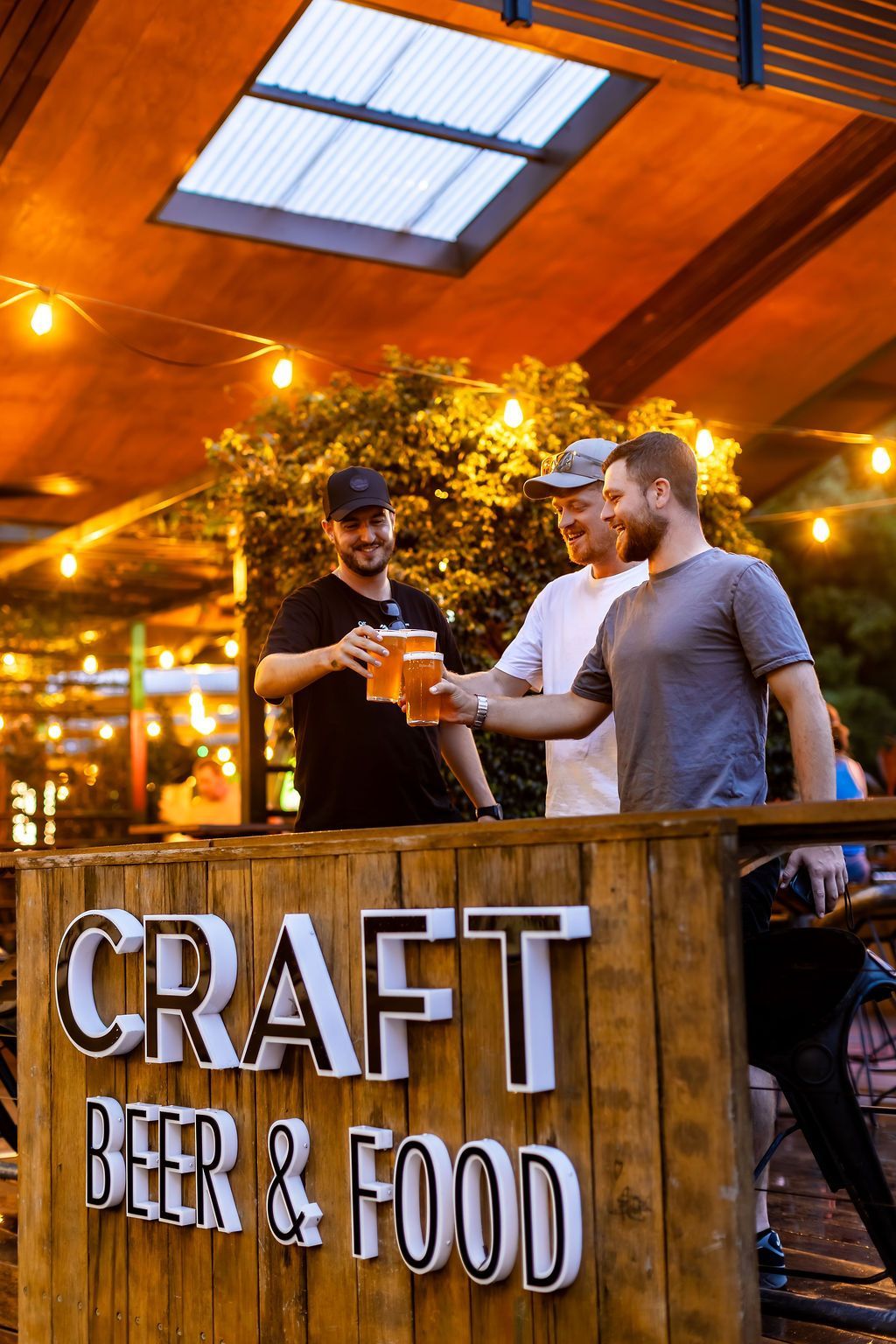 Woman and man eating outdoors. Woman in pink top, man in hat, beer bottle on table.