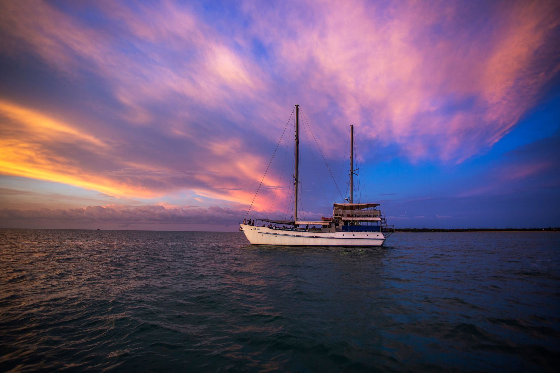 Boat on calm water under a vibrant sunset with pink, purple, and blue clouds.