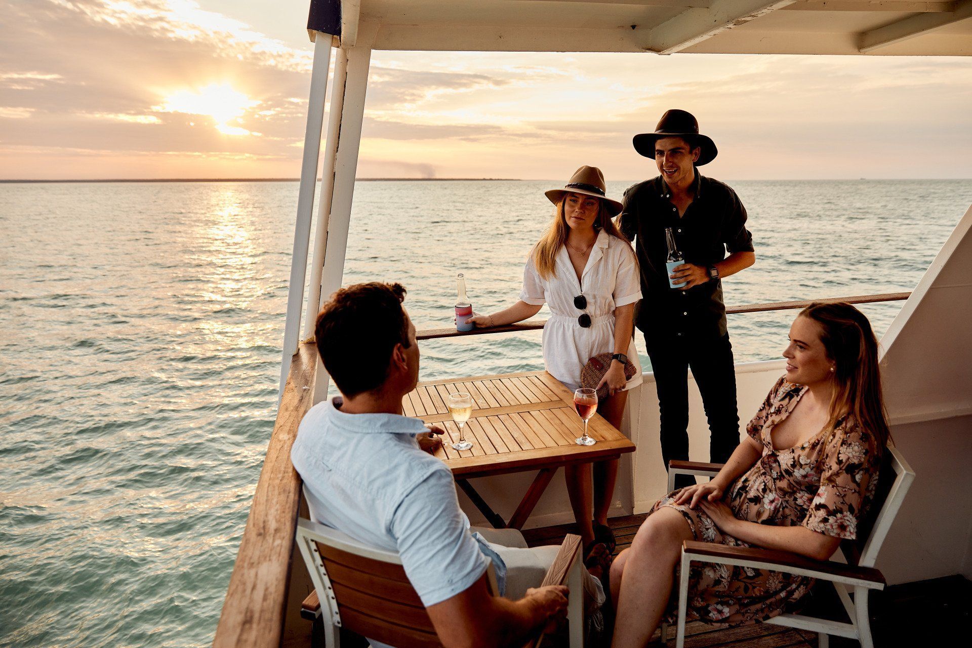 Four people enjoying drinks on a deck overlooking the ocean at sunset.