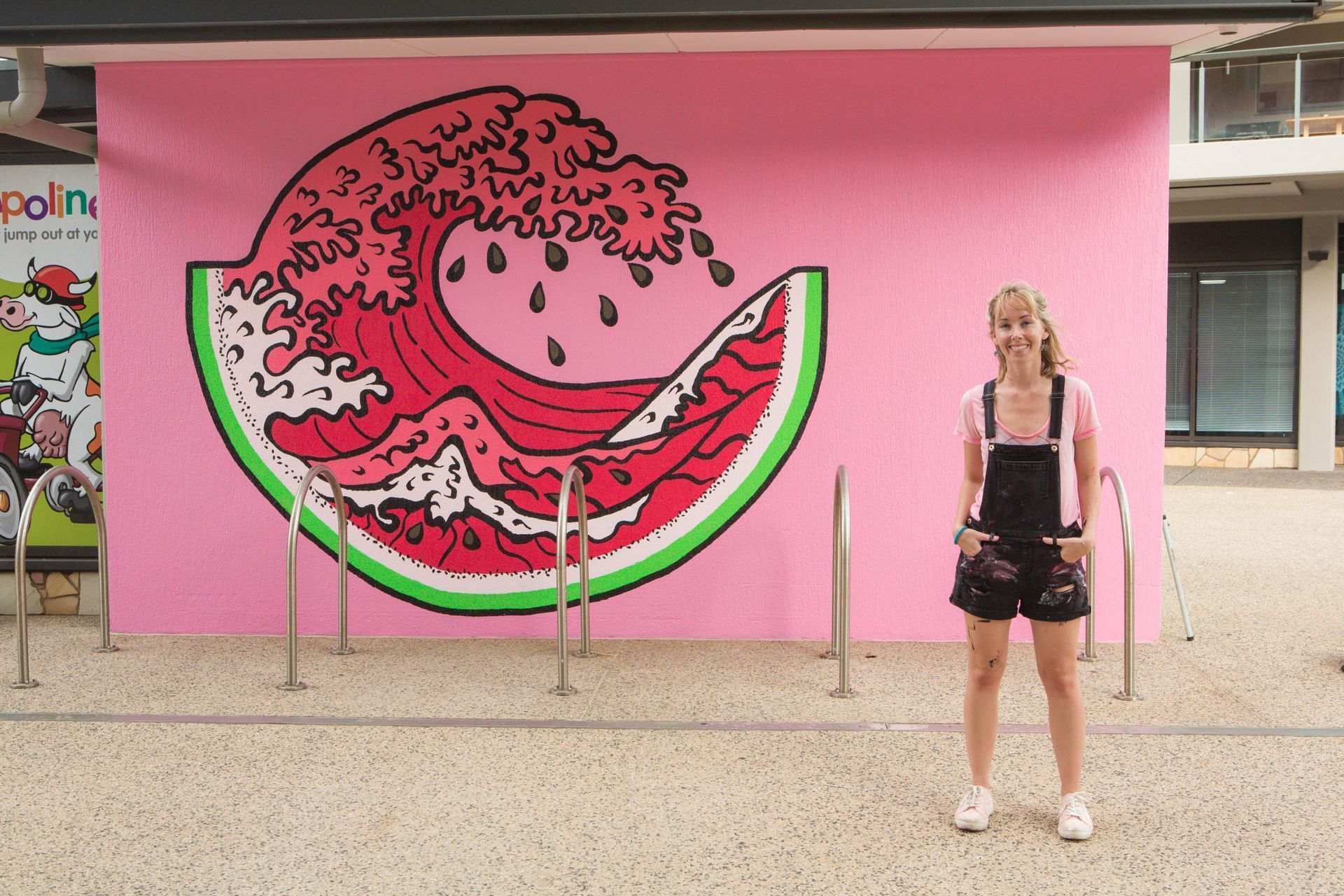 Woman standing in front of a watermelon-wave mural on a pink wall; bike racks in front.