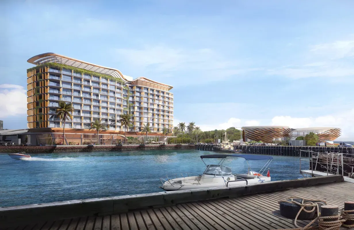 Hotel on waterfront with boats in harbor under blue sky.